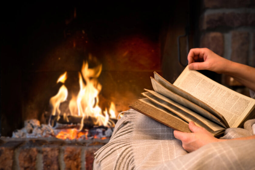 person reading a book infront of a fire