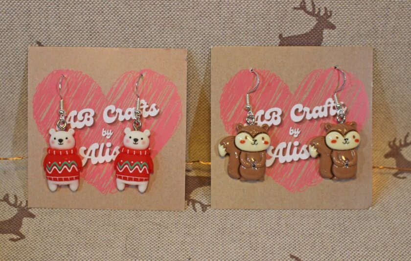 Earrings are displayed on two cards with heart designs. One pair features polar bears in red sweaters, and the other pair features squirrels. Both cards have AB Crafts by Alison written in a playful font.
