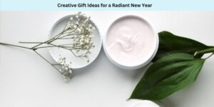 An open jar of pink cream with white lid, beside sprigs of white flowers and green leaves on a white surface. Text above reads Creative Gift Ideas for a Radiant New Year.