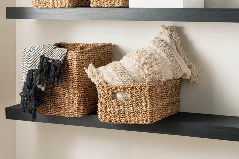 Two woven baskets on a dark shelf; one holds a textured cushion, the other has a black-and-white patterned throw draped over the side. The soft colors create a cozy, minimalist aesthetic.