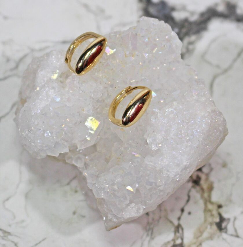 Gold earrings with teardrop-shaped design rest on a glittering white geode slice, which is set against a marble background.
