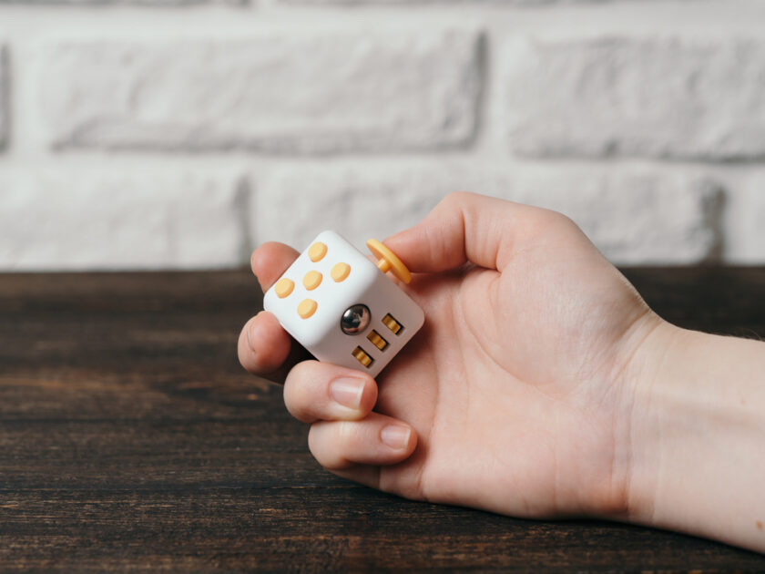 Fidget cube stress reliever in hand over brown wooden background. Fingers antistress toy in hand