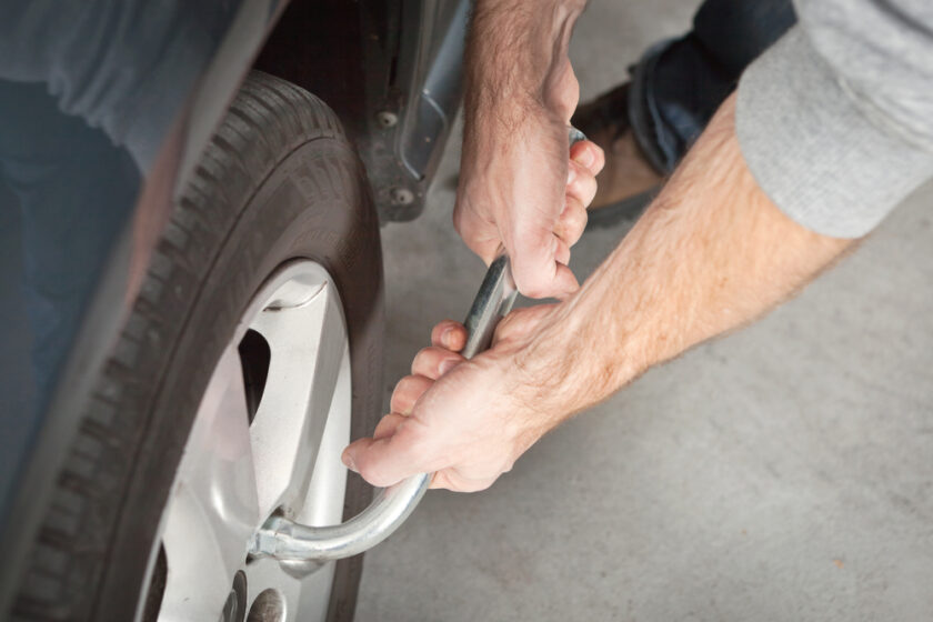A person is using a tire iron to change a car tire. The hands are gripping the tool, loosening or tightening lug nuts on the wheel, with part of the cars body visible. The focus is on the hands and the wheel.