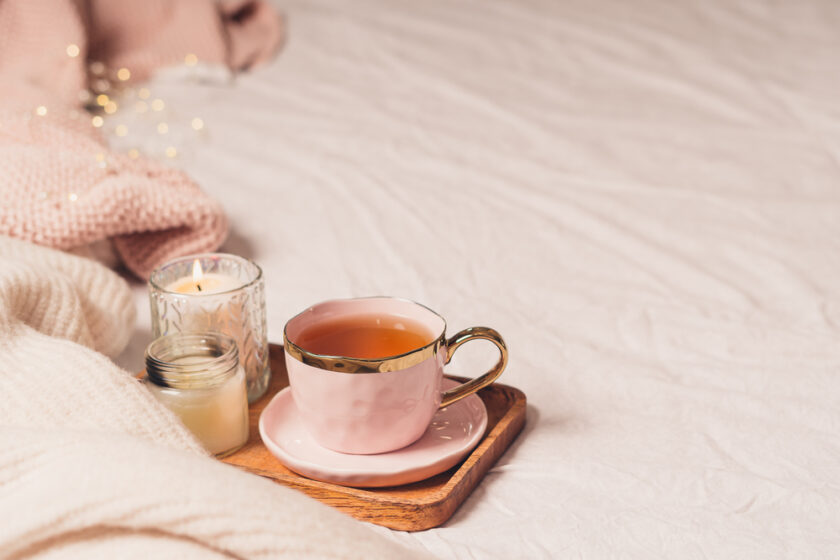 Details of still life in the home interior of living room. Sweater, cup of tea, cotton, cozy, book, candle. Moody. Cosy autumn winter concept. Decoration, vintage with glow bokeh.