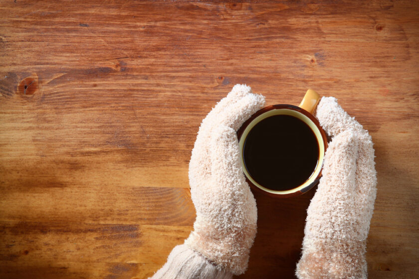 Person wearing gloves with hands around a cuppa