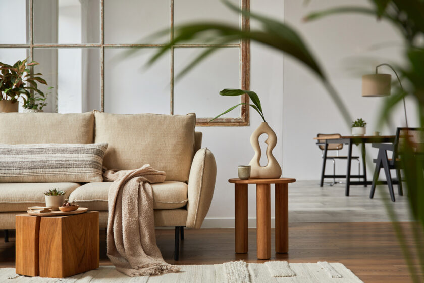 Modern living room interior design with beige sofa, wooden side table, plants and creative accessories. 