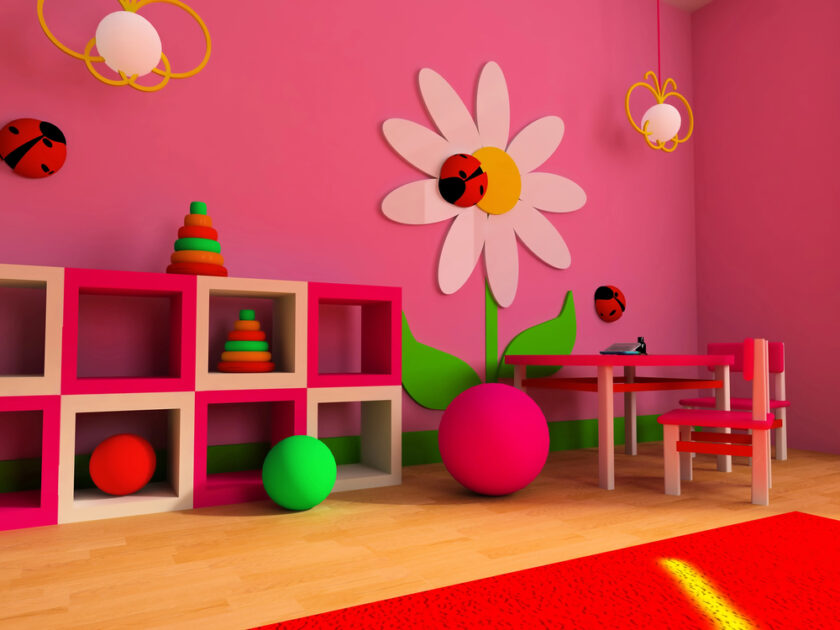 A colorful childrens playroom with pink walls and a white daisy mural adorned with ladybugs. The room has pink and white shelves holding toys, a small table and chair, and a red carpet on a wooden floor. Various colorful balls are scattered around.