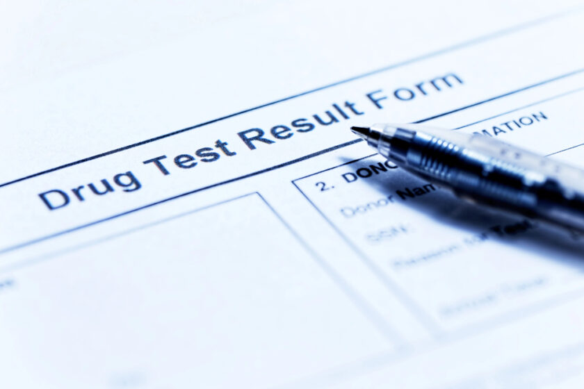 Close-up of a drug test result form with a pen resting on top. The form is partially visible, showing the printed text Drug Test Result Form and some blank fields for information. The image has a blue tint.