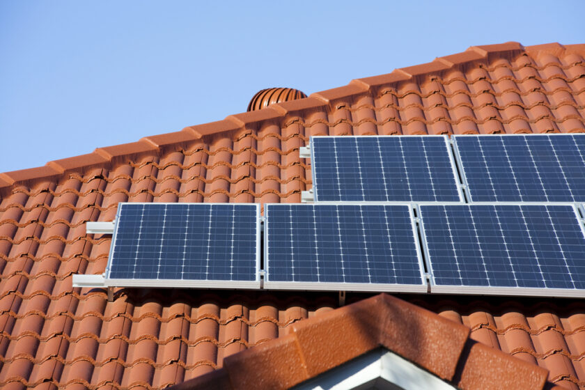 Solar panels installed on a red tiled roof under a clear blue sky.