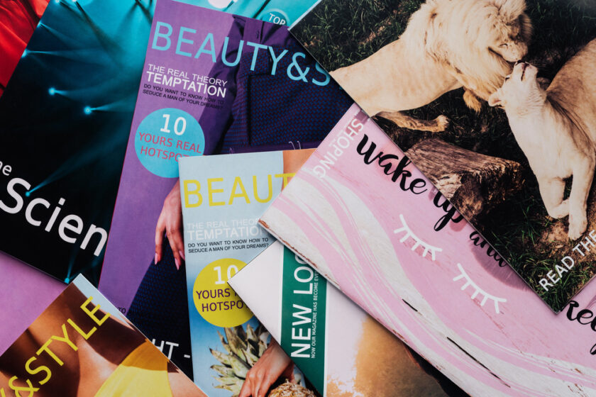A scattered arrangement of colorful fashion and lifestyle magazines, with covers featuring text about beauty, style, temptation, and health, along with partial images of people and animals.