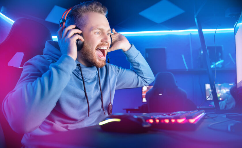 Streamer young man rejoices in victory professional gamer playing online games computer with headphones, neon color.