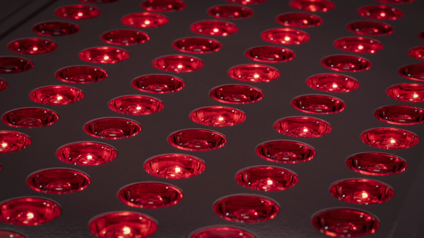 A grid of glowing red LED lights embedded in round, reflective sockets on a dark surface. The lights are evenly spaced, creating a repetitive pattern across the image.