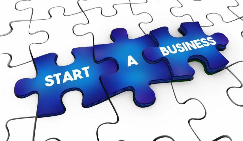 Three blue puzzle pieces with the words START A BUSINESS on them are connected, lying on top of white puzzle pieces, symbolizing the concept of starting a business as part of a bigger picture.