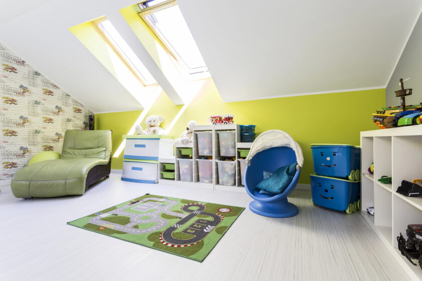 Bright childrens playroom with green walls, skylights, a green lounge chair, toys on shelves, stacked blue storage bins, a car-track rug, and a blue egg chair. Stuffed toys and bins are neatly organized.