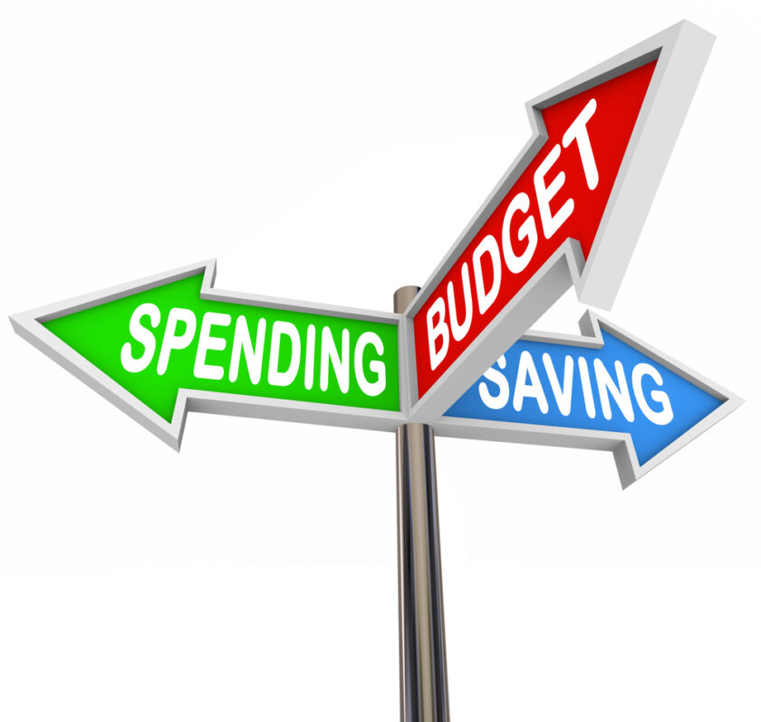 Three arrows on a signpost point in different directions, labeled SPENDING (green), BUDGET (red), and SAVING (blue), representing financial decision-making options.