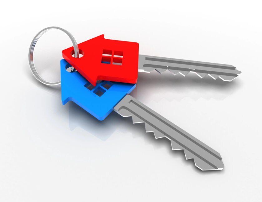 Two silver keys on a metal keyring, each with a house-shaped key cover—one red and one blue—against a white background.