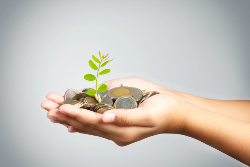 Two hands gently holding a pile of coins with a small green plant sprouting from the center, symbolizing financial growth and investment.