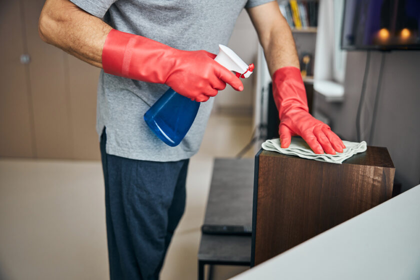 Cropped photo of man wearing rubber gloves and spraying cleaning liquid on the surfaces and wiping them