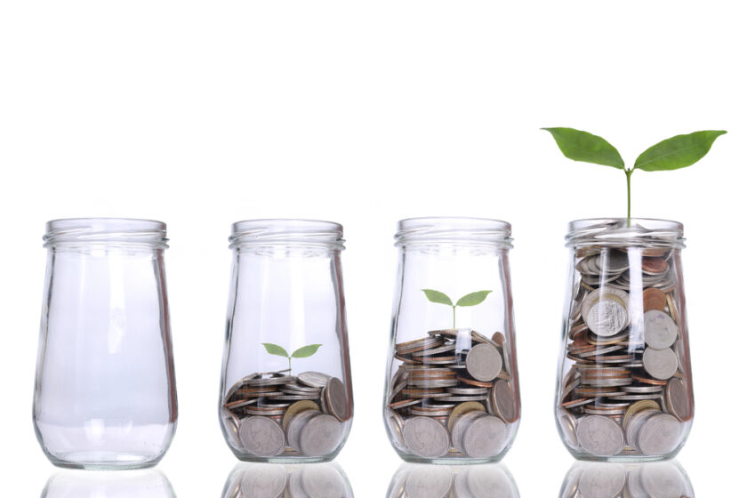 Four glass jars in a row: the first is empty, the next two gradually fill with coins and show small green sprouts, and the last jar is full of coins with a larger plant growing from it.