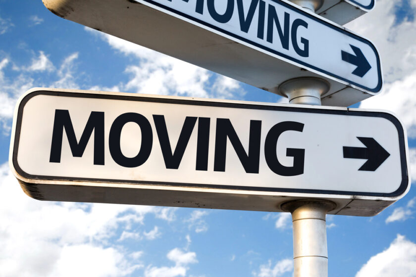A street sign with the word MOVING and a right-pointing arrow, set against a blue sky with scattered white clouds.