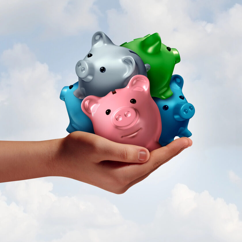 A hand holds four colorful piggy banks—pink, blue, green, and silver—against a cloudy sky background, symbolizing savings or financial management.