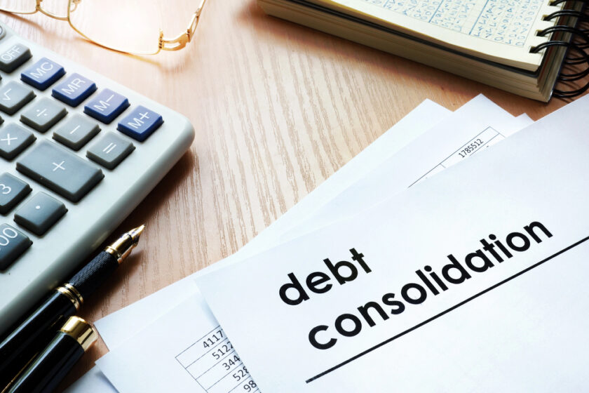 A document labeled debt consolidation lies on a desk next to a pen, calculator, and a notebook with handwritten notes.