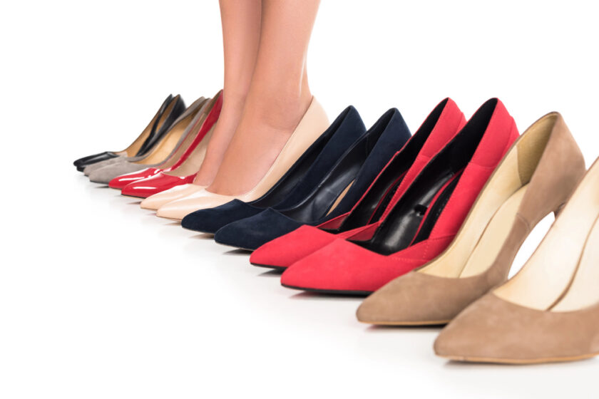 A person standing in front of a row of high-heeled shoes in various colors and styles, arranged neatly on a white background.