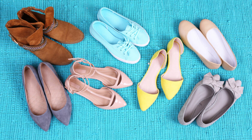 Six pairs of women’s shoes in various styles and colors, including boots, sneakers, flats, and heels, are arranged in a circle on a blue textured rug.