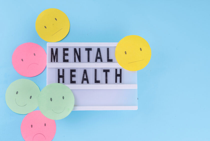 A lightbox displaying the words MENTAL HEALTH is surrounded by colorful paper circles with happy, sad, and neutral faces on a blue background.