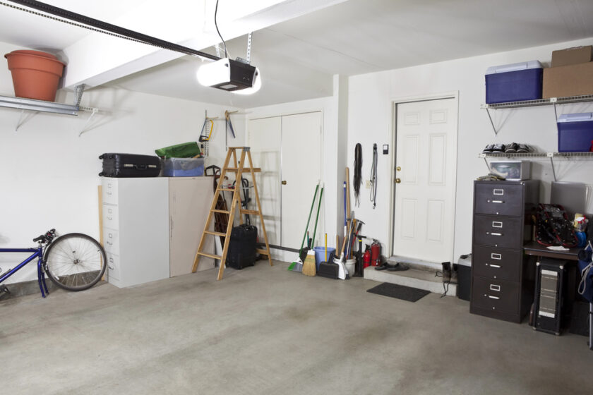 A clean, organized garage with shelves, cabinets, a ladder, cleaning supplies, storage bins, a blue bicycle, and a filing cabinet. The floor is clear and there are two white doors on the back wall.