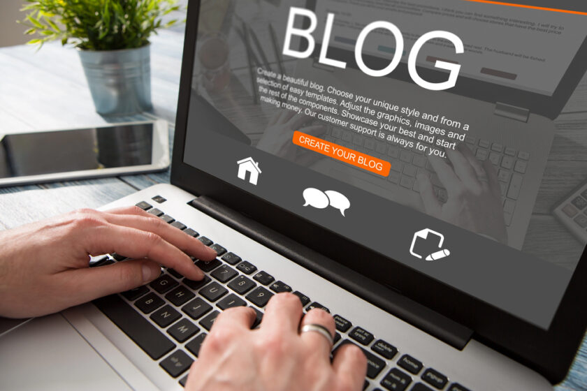 Person typing on a laptop, with a screen displaying the word BLOG and options to create a blog. Various icons and a button labeled CREATE YOUR BLOG are visible on the screen.