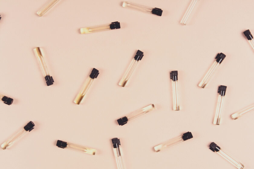 Small glass vials with black caps, some filled with a yellowish liquid and others empty, are scattered on a light peach-coloured surface.
