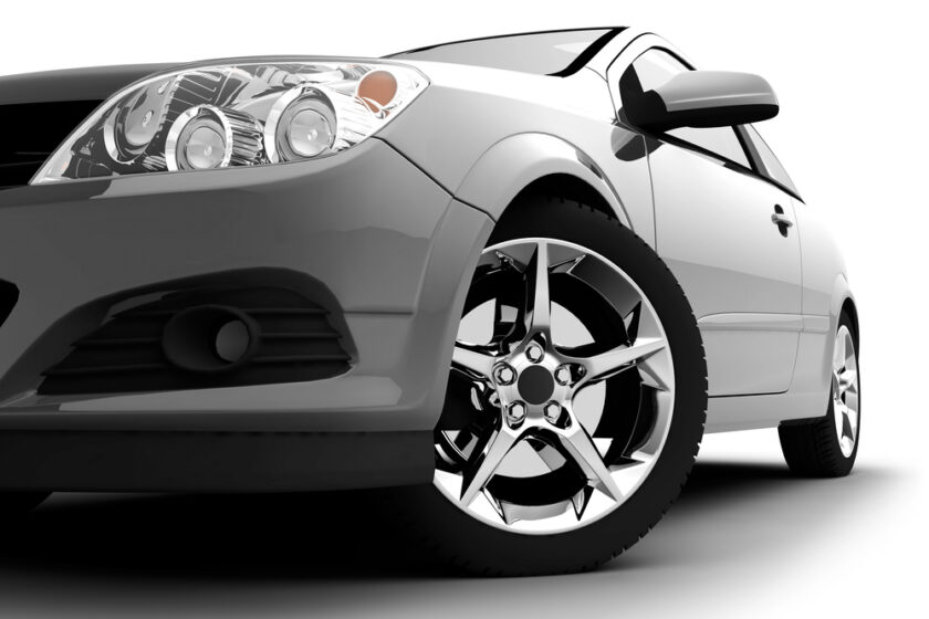Close-up view of the front side of a modern silver car, focusing on the shiny chrome wheel and headlamp, set against a white background.