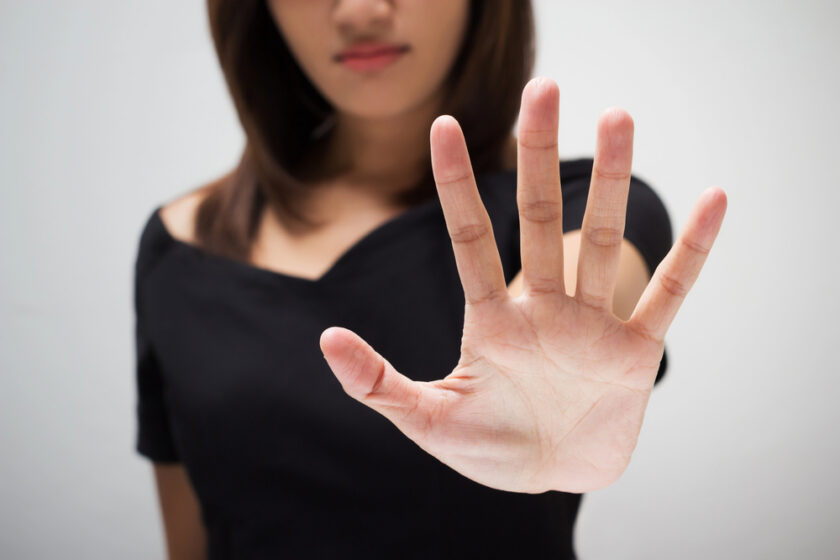 A woman in a black top holds her hand up with her palm facing the camera, signalling stop or refusal. Her face is partially out of focus.