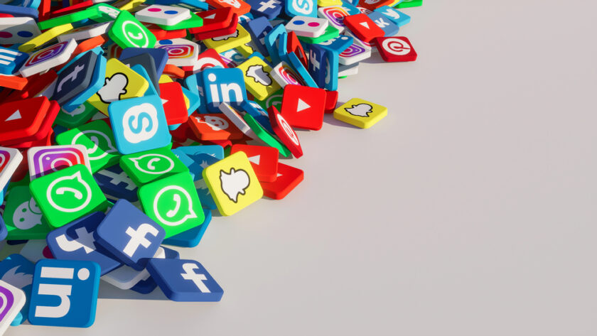 A pile of colourful 3D cubes featuring various popular social media app logos, such as Facebook, Twitter, Instagram, Snapchat, LinkedIn, WhatsApp, and YouTube, scattered on a white surface.
