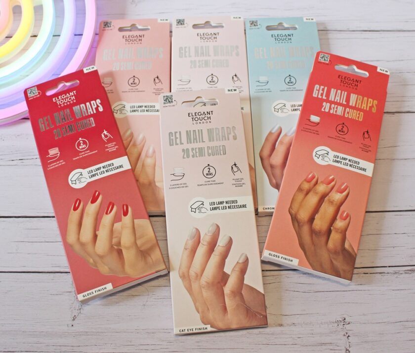 Six boxed packages of Elegant Touch Gel Nail Wraps are arranged on a white wooden surface. The boxes display hands with manicured nails in various colours and include product details. A rainbow-shaped object is partially visible.