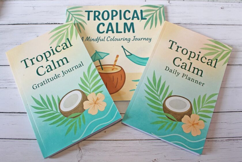 Three books with tropical-themed covers are arranged on a white wooden surface. Titles include Tropical Calm Gratitude Journal, Tropical Calm Daily Planner, and Tropical Calm: A Mindful Colouring Journey.