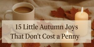 A cup of coffee, two lit candles, and autumn leaves on a cosy beige blanket, with the text 15 Little Autumn Joys That Don’t Cost a Penny overlaid in the centre.