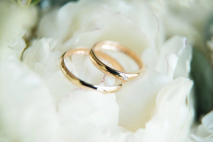 Two gold wedding rings, one with a small diamond, rest on soft white flower petals, creating a romantic and elegant scene.