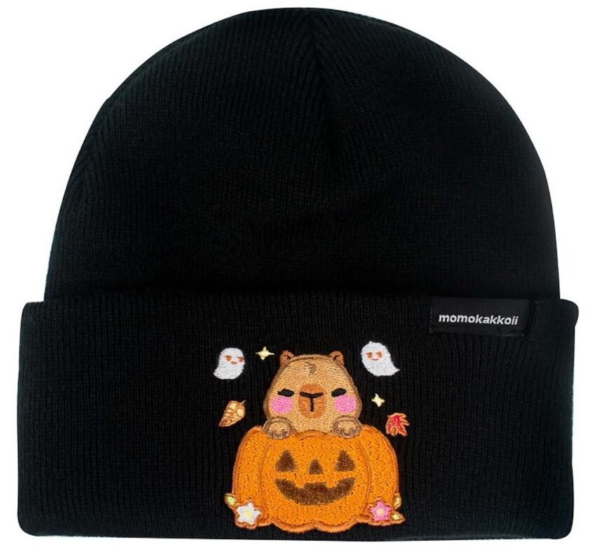 A black beanie with an embroidered design featuring a cute brown bear sitting on a carved jack-o'-lantern, surrounded by two white ghosts, leaves, and stars. A small momokakkoii label is on the cuff.