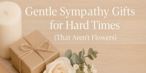 A candle, a gift wrapped in brown paper with string, and white flowers sit on a wooden surface. Text reads: Gentle Sympathy Gifts for Hard Times (That Aren’t Flowers).