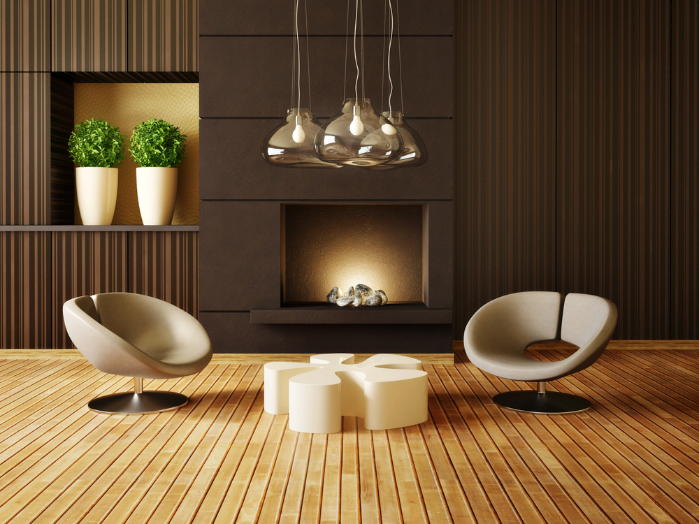 A modern living room with wood-panelled walls, two round grey chairs, a sculptural white coffee table, a fireplace, hanging pendant lights, and two tall white planters with green plants on a wooden floor.