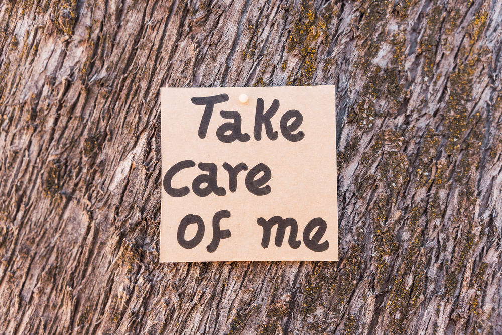A handwritten note saying Take care of me is pinned to tree bark, conveying a message of care or concern.