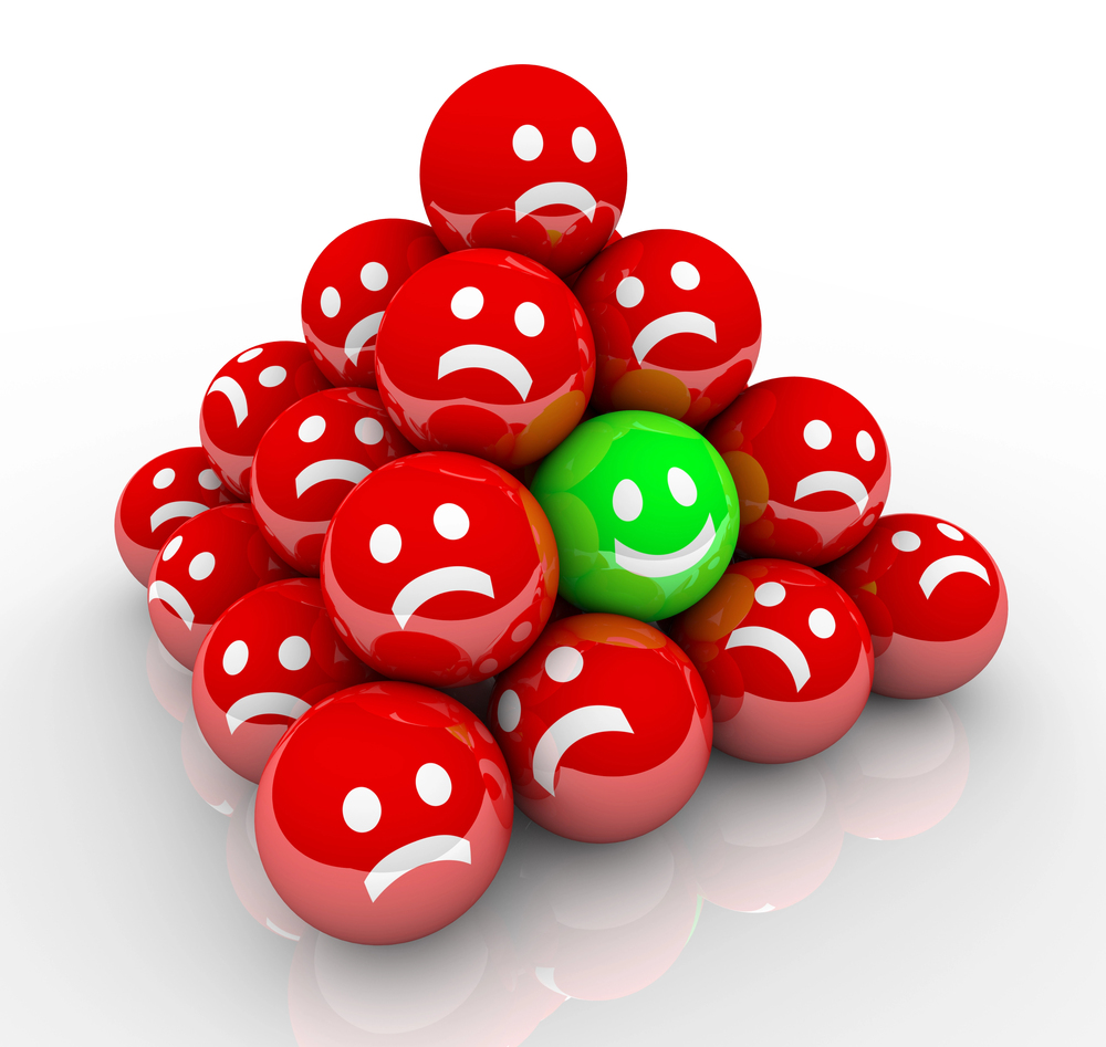 A pyramid of red balls with sad faces, except for one green ball near the centre that has a happy face. The balls are arranged in a cluster on a white background.