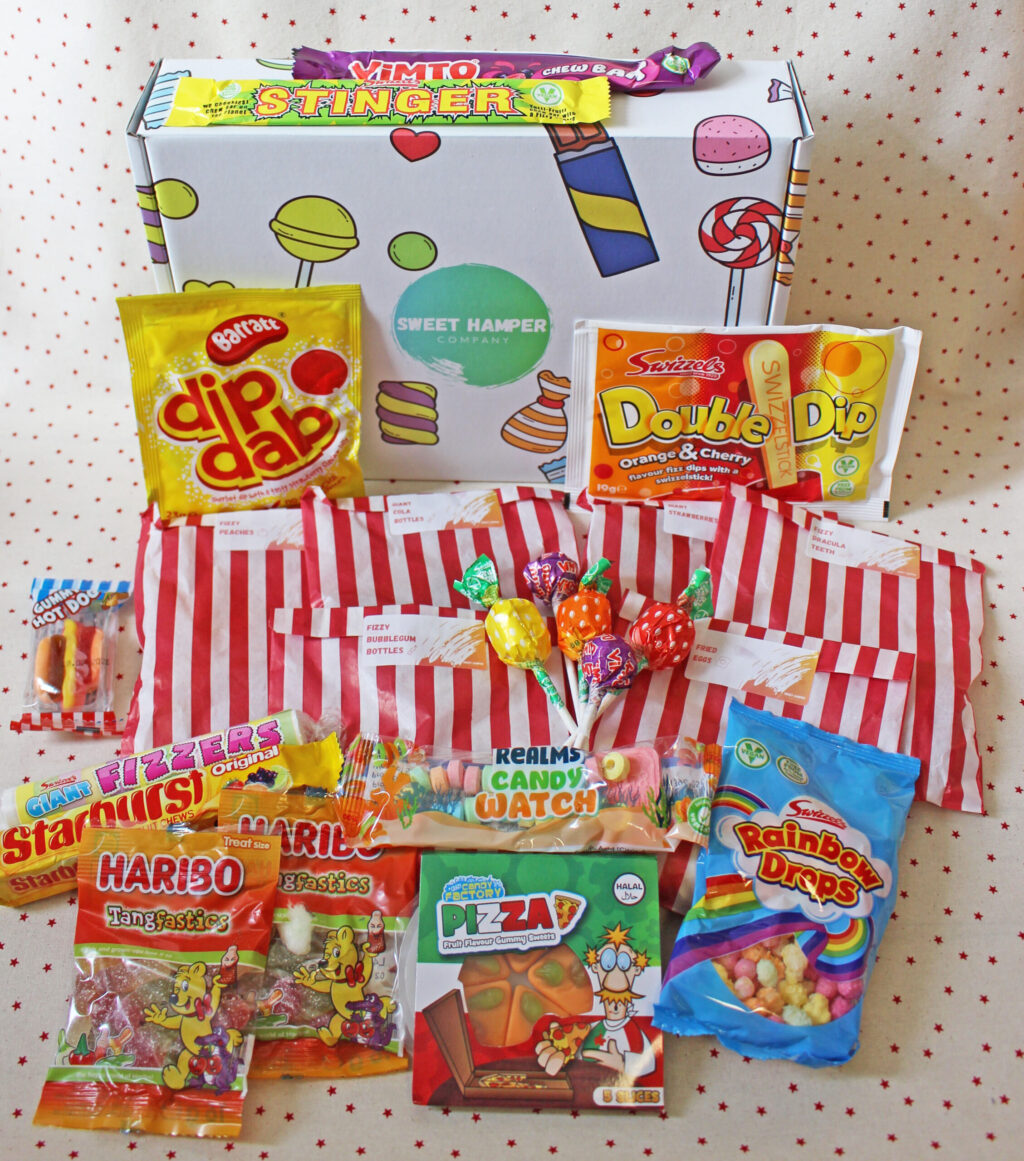 A selection of colourful retro sweets, including lollipops, Haribo, Dip Dab, Double Dip, Rainbow Drops, and more, arranged in front of a white sweet-themed box labelled Sweet Hamper.