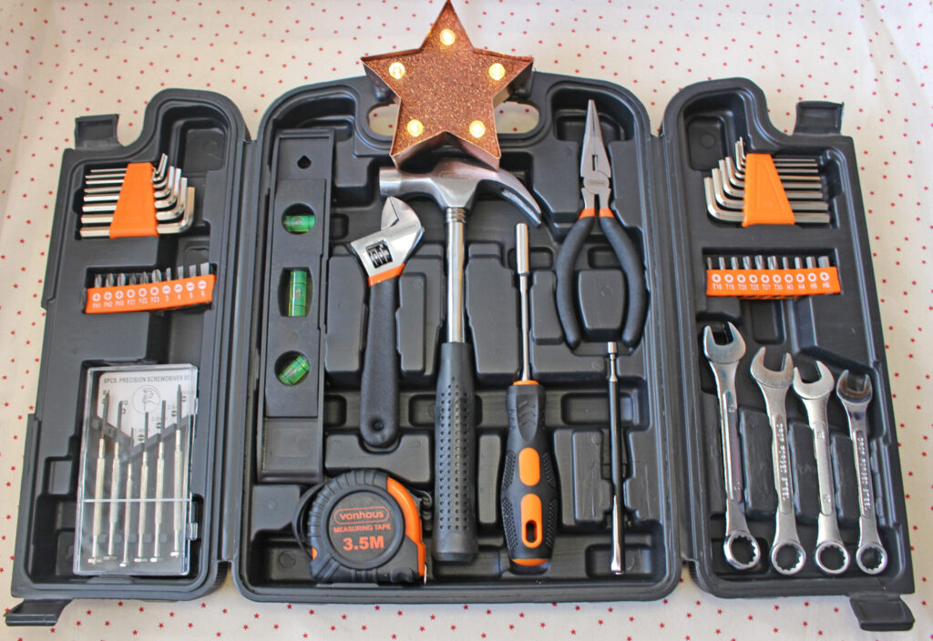 A black tool kit with various tools neatly arranged, including a hammer, pliers, screwdrivers, spanner set, tape measure, Allen keys, and drill bits. A star-shaped light sits on top of the kit.