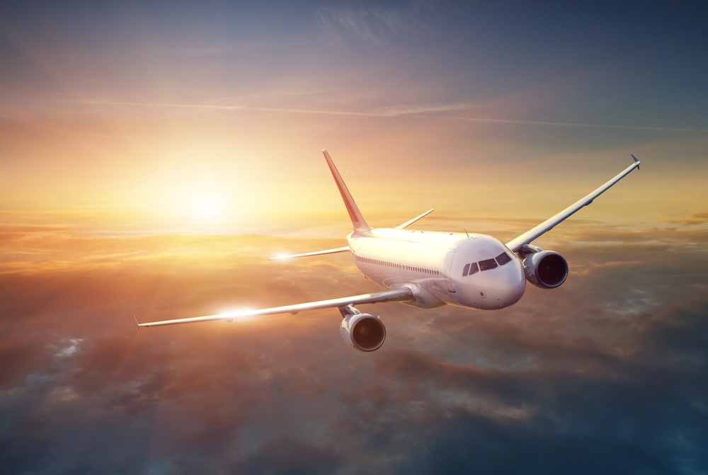 A commercial aeroplane flying above the clouds during sunset, with warm sunlight illuminating the sky and the aircraft's wings.