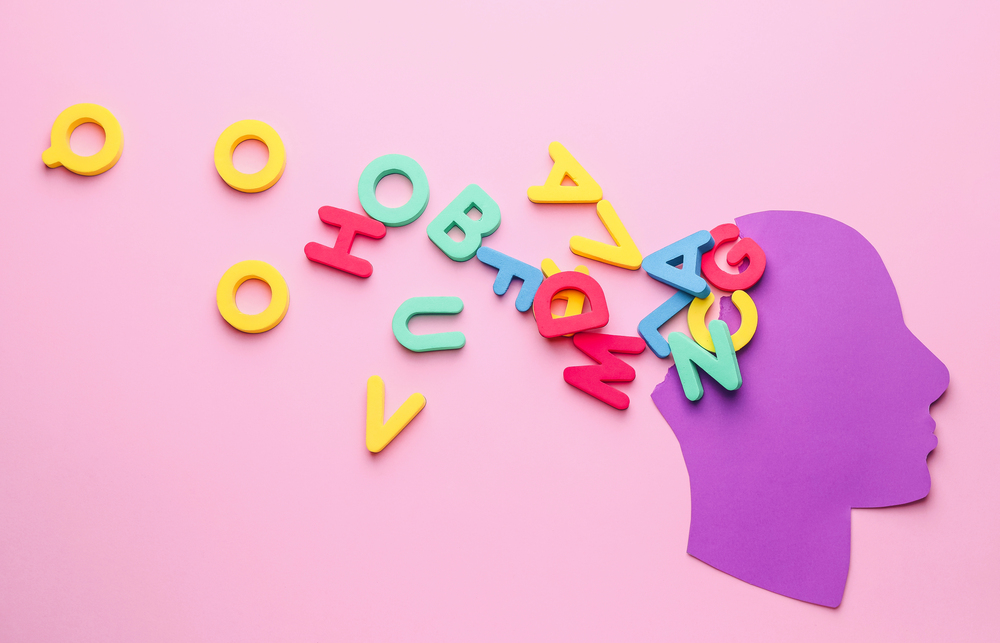A purple paper cut-out of a human head on a pink background with colourful letters and numbers spilling out from the top, symbolising learning, creativity, or ideas.
