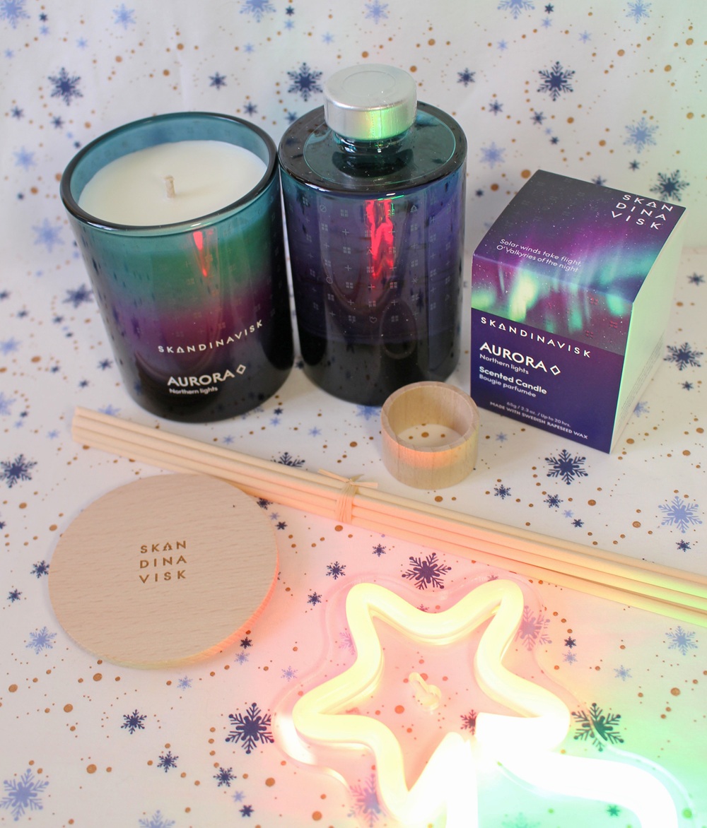 Aurora-themed Skandinavisk candle, diffuser, box, coaster, matches, and neon star light arranged on a snowflake-patterned background.
