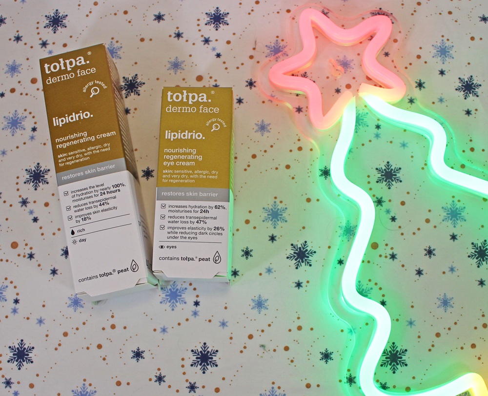 Two boxes of Tolpa dermo face lipidrio nourishing regenerating creams on a snowflake-patterned background, beside a neon light shaped like a Christmas tree with a star.